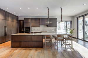 Kitchen featuring modern cabinets, light wood finished floors, a large island with sink, light stone countertops, and decorative light fixtures