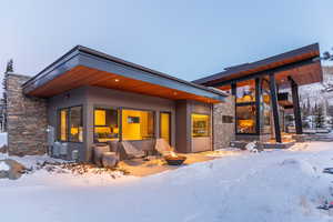 Snow covered property with stone siding, an outdoor fire pit, a patio, and stucco siding