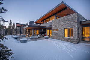 Snow covered back of property with a patio, a balcony, and stone siding