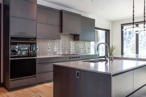 Kitchen with dark wood finish cabinets, light wood-style floors, an island with sink, decorative light fixtures, and modern cabinets