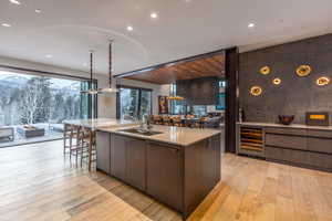 Kitchen with light wood-style flooring, wine cooler, a large island with sink, and modern cabinets