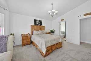 Bedroom with vaulted ceiling, light carpet, suspended lighting, and ensuite bathroom