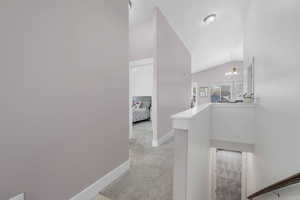 Corridor featuring hanging lights, light colored carpet, lofted ceiling, and an upstairs landing