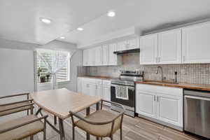 Kitchen featuring white cabinets, stainless steel appliances, backsplash, dark stone countertops, and recessed lighting