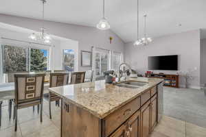 Kitchen with suspended lighting, light stone counters, vaulted ceiling, wood finish cabinets, and a center island with sink