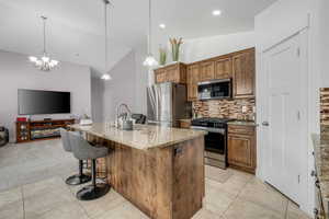 Kitchen featuring light stone countertops, stainless steel appliances, wood finish cabinetry, open floor plan, and an island with sink