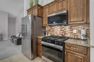 Kitchen featuring stainless steel appliances, light stone countertops, light carpet, wood finish cabinets, and light tile patterned floors