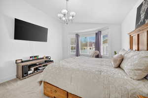 Bedroom featuring vaulted ceiling, light carpet, and a chandelier