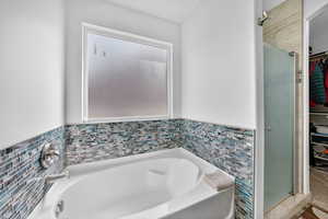 Bathroom featuring a walk in closet, a garden tub, a shower stall, tile walls, and a wainscoted wall