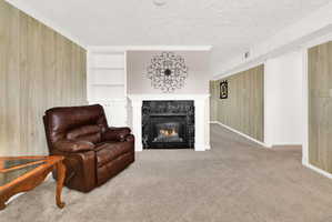 Sitting room with wooden walls, built in shelves, a fireplace, crown molding, and light carpet