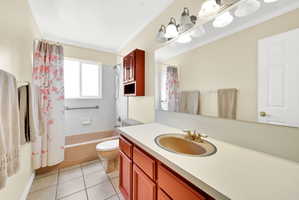 Bathroom featuring vanity, shower / bath combo, light tile patterned floors, and ornamental molding