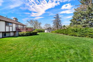 View of green lawn with a storage shed and a wooden deck