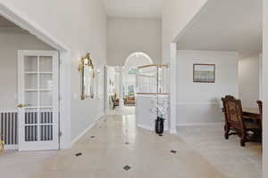 Hall featuring a high ceiling, light colored carpet, light tile patterned floors, and arched walkways