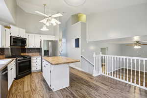 Kitchen featuring ceiling fan, a high ceiling, stainless steel appliances, light wood-style floors, and white cabinetry