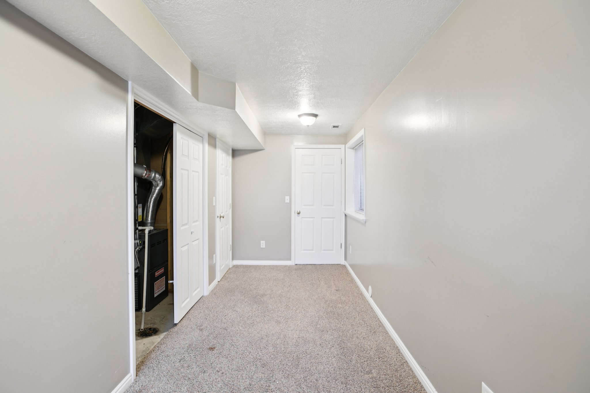 Hallway with a textured ceiling, light colored carpet, and heating unit
