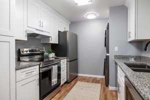 Kitchen with stainless steel appliances, white cabinets, dark stone countertops, and dark wood-style flooring