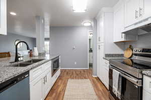 Kitchen featuring stainless steel electric range oven, light stone countertops, white cabinetry, and dishwashing machine