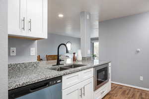 Kitchen with light stone countertops, white cabinetry, stainless steel dishwasher, built in microwave, and dark wood-type flooring