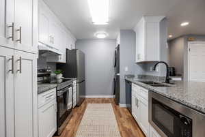 Kitchen featuring stainless steel appliances, dark stone countertops, white cabinetry, stacked washing machine and dryer, and light wood-style floors