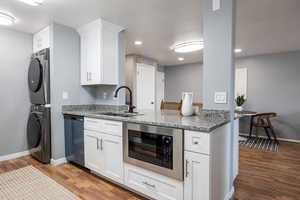 Kitchen with white cabinets, stainless steel microwave, light stone countertops, stacked washer / drying machine, and recessed lighting