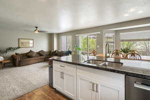 Kitchen featuring a textured ceiling, white cabinetry, dark stone counters, dishwasher, and dark wood-type flooring