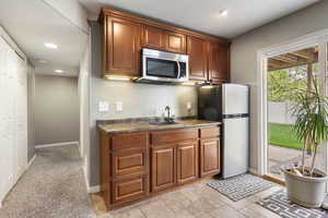 Kitchen featuring stainless steel appliances, dark countertops, stone tile flooring, wood finish cabinetry, and recessed lighting