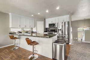 Kitchen with a kitchen breakfast bar, stainless steel appliances, white cabinets, a peninsula, and dark wood-style flooring