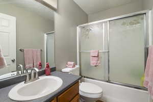 Bathroom featuring vanity, shower / bath combination with glass door, and a textured ceiling
