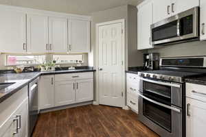 Kitchen with stainless steel appliances, a textured ceiling, white cabinets, and dark wood-style floors