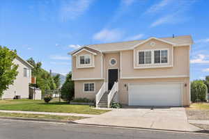 Raised ranch with stucco siding, a front yard, a garage, concrete driveway, and roof with shingles