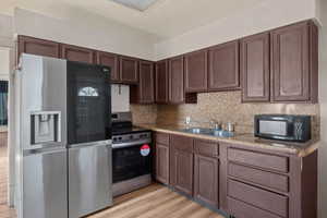 Kitchen featuring stainless steel appliances, light wood finished floors, backsplash, and dark wood finish cabinetry