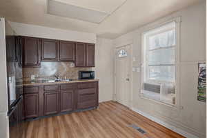 Kitchen featuring dark wood finish cabinets, light wood finished floors, light countertops, refrigerator with ice dispenser, and backsplash