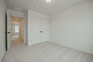 Unfurnished bedroom with light carpet and a closet