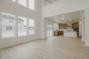 Unfurnished living room featuring light wood finished floors, recessed lighting, plenty of natural light, and a high ceiling