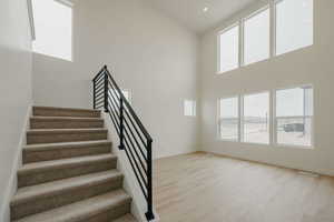 Staircase with healthy amount of natural light, wood finished floors, a high ceiling, and recessed lighting