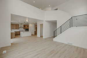 Unfurnished living room with light wood finished floors, recessed lighting, and a high ceiling