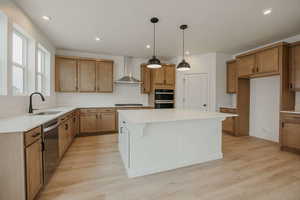Kitchen with wood finish cabinetry, a kitchen island, light wood-style floors, stainless steel dishwasher, and pendant lighting