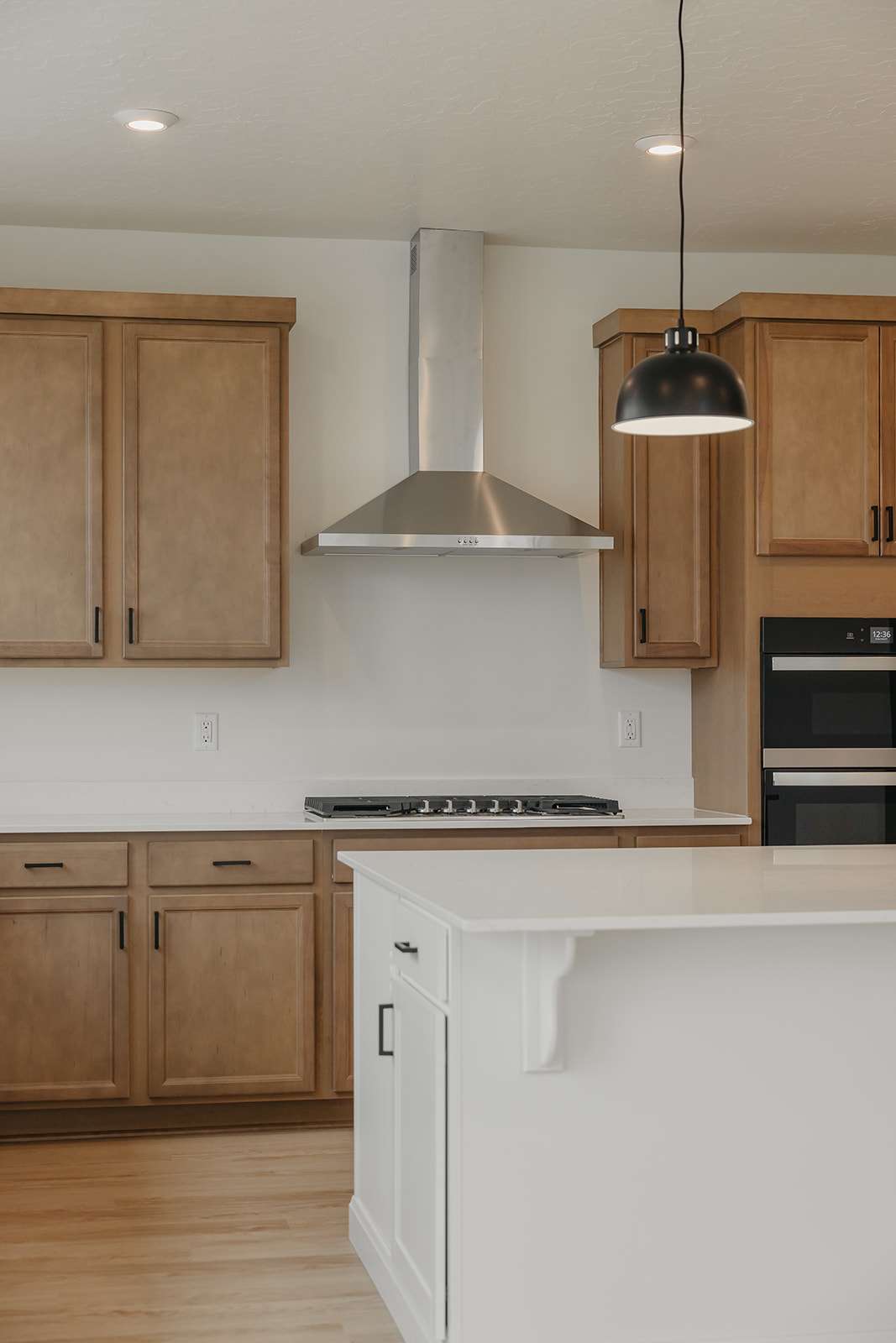Kitchen featuring two tone cabinetry, pendant lighting, stainless steel appliances, light wood-style floors, and light stone countertops