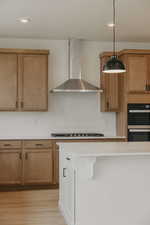 Kitchen featuring two tone cabinetry, pendant lighting, stainless steel appliances, light wood-style floors, and light stone countertops