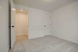 Unfurnished bedroom with light carpet and baseboards