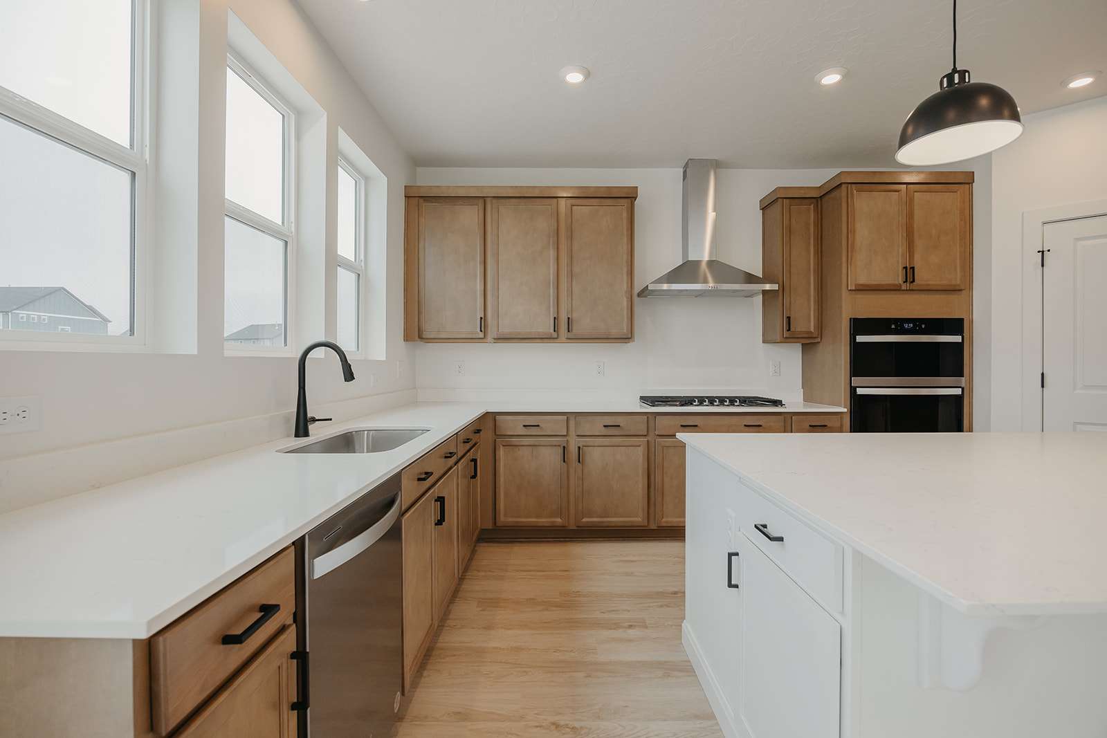 Kitchen with two tone cabinets, light stone countertops, black appliances, light wood finished floors, and decorative light fixtures