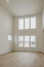 Unfurnished room featuring a high ceiling, light wood finished floors, recessed lighting, and healthy amount of natural light