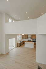 Unfurnished living room featuring a high ceiling, light wood-style floors, and recessed lighting