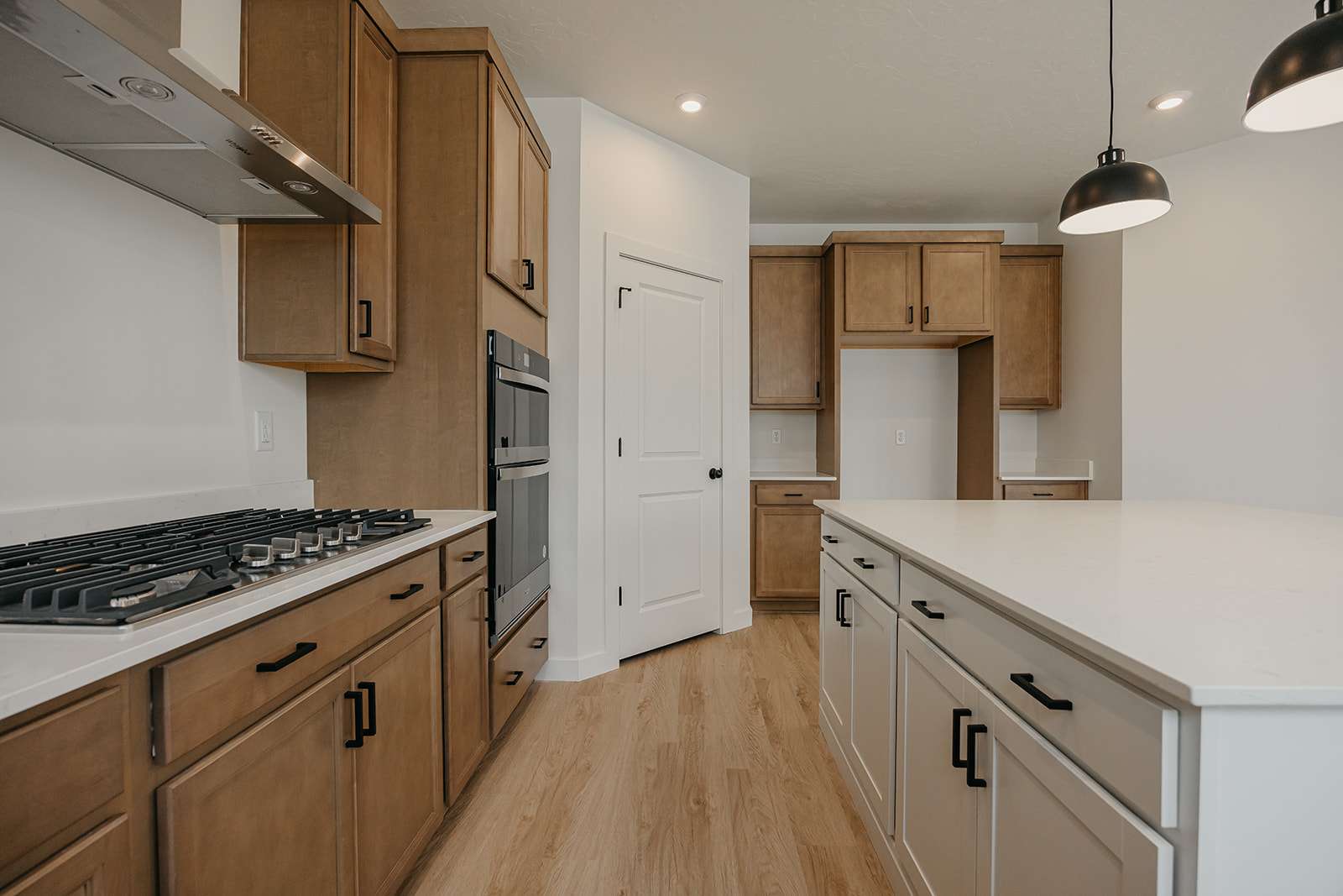 Dual tone kitchen with light wood-style flooring, stainless steel appliances, decorative light fixtures, a center island, and light stone countertops