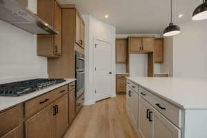 Dual tone kitchen with light wood-style flooring, stainless steel appliances, decorative light fixtures, a center island, and light stone countertops