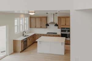 Kitchen with black appliances, pendant lighting, a kitchen island, light wood-type flooring, and wood finish cabinetry