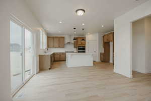 Kitchen featuring wood finish cabinetry, a kitchen island, light wood finished floors, decorative light fixtures, and a kitchen breakfast bar