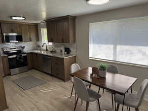 Kitchen with stainless steel appliances, light stone counters, a textured ceiling, decorative backsplash, and light wood-type flooring