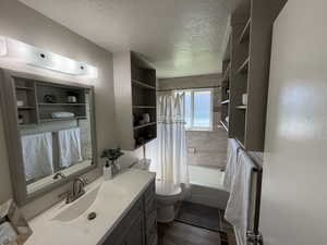 Bathroom featuring vanity, shower / tub combo, a textured ceiling, a textured wall, and dark wood finished floors