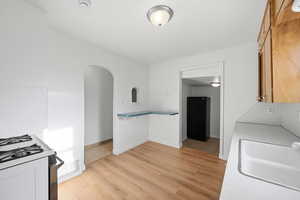Kitchen with freestanding refrigerator, arched walkways, light wood-type flooring, white gas range, and light countertops